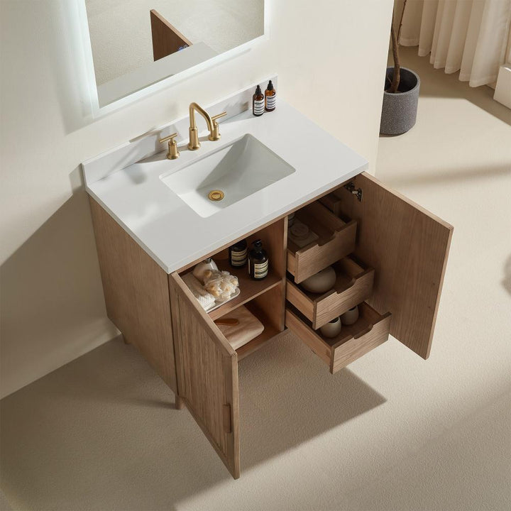 The Liora 30 Inch Bathroom Vanity features a white sink, gold faucet, and open wooden cabinet doors revealing organized shelves and drawers for towels, bottles, and containers, all set on a light-colored floor.
