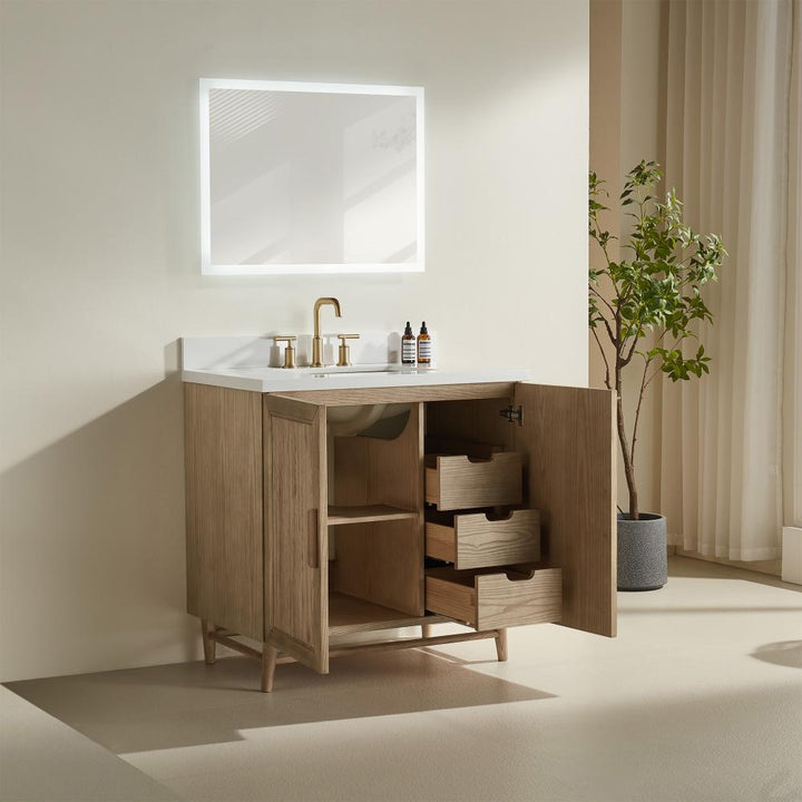 A modern bathroom showcases the Liora 30 Inch Bathroom Vanity with open cabinet doors, drawers, a white countertop with gold fixtures, a backlit mirror, and a potted plant in the corner.