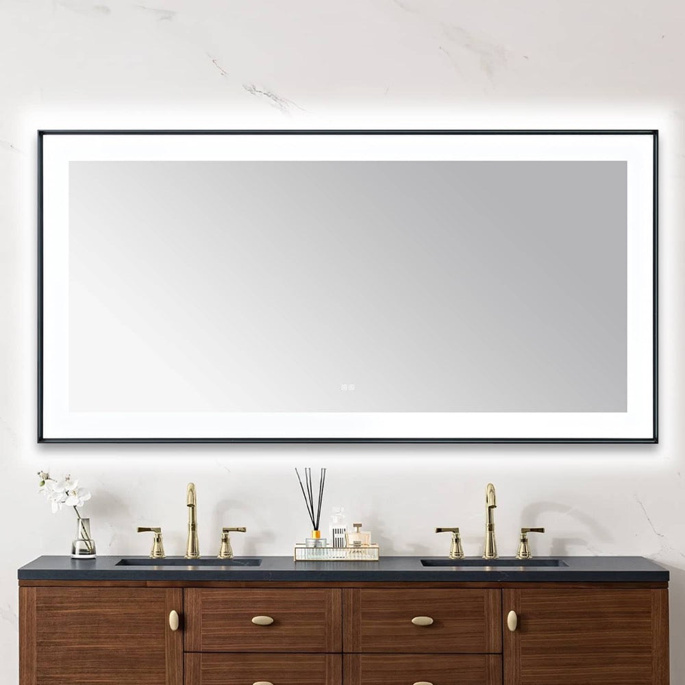 A modern bathroom features the Lexington 72 inch x 36 inch LED Lighted Slim Frame Mirror above a double sink vanity with brass faucets, wooden cabinets, and toiletries neatly arranged on the countertop.