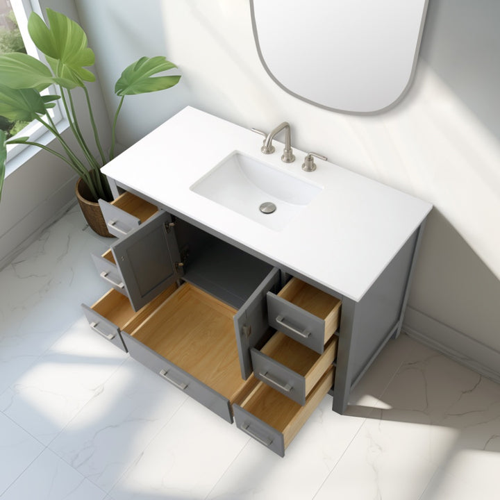 The Vanea 48 inch Bathroom Vanity in Gray with White Quartz Top features a built-in sink, silver faucet, elegant gray cabinetry with open doors and drawers revealing empty wooden interiors. A green plant is placed nearby.