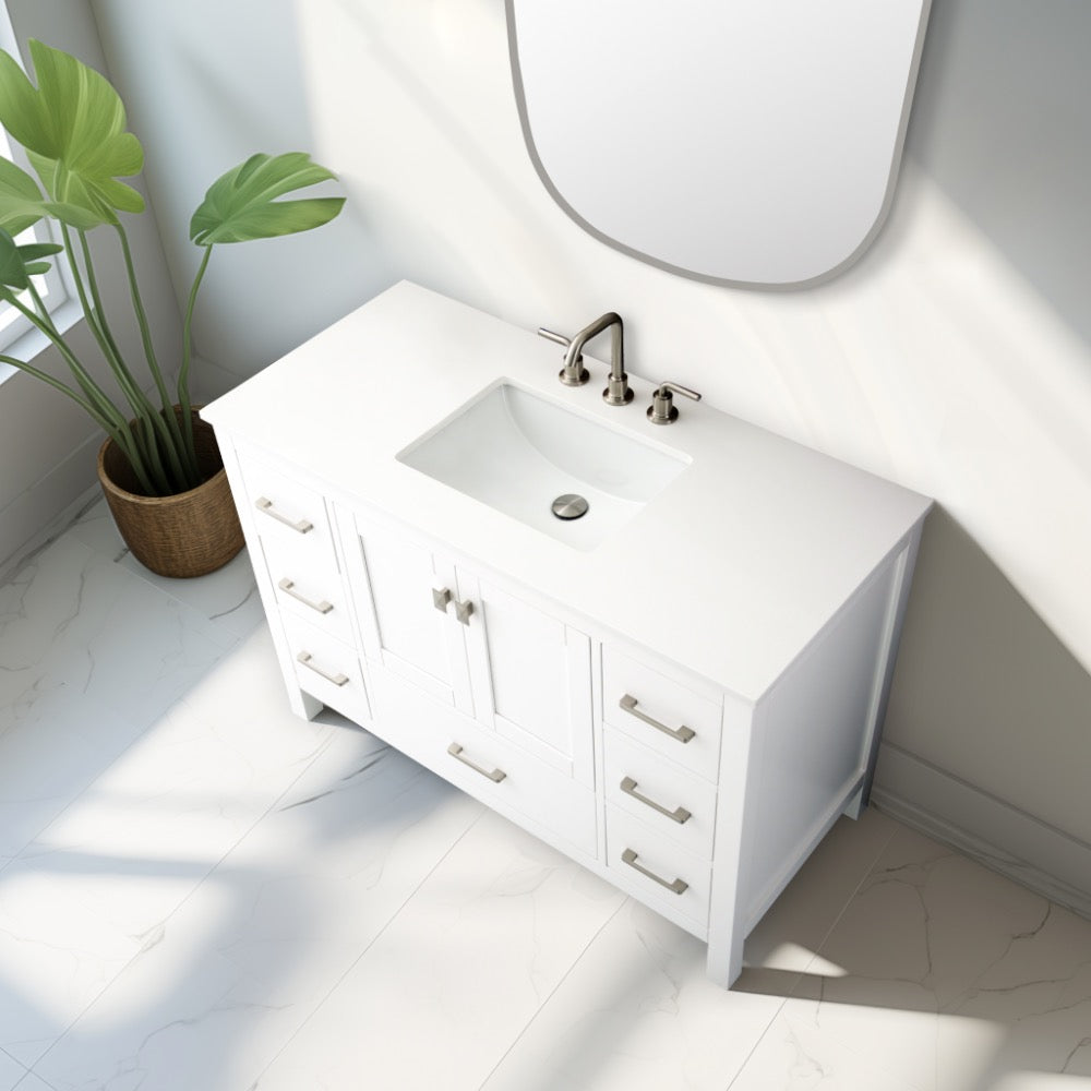 A Vanea 48 inch Bathroom Vanity in White with a white quartz top stands against a white wall beside a large green potted plant as sunlight streams through the window onto the tiled floor.