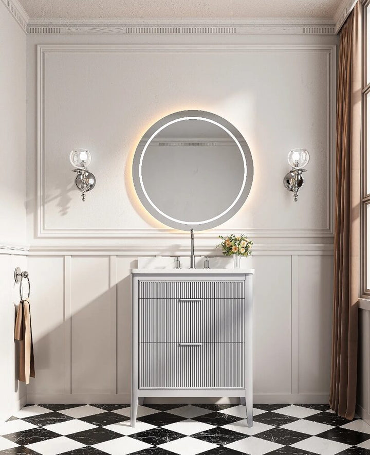 A stylish bathroom with black-and-white checkered floor, white wainscoting, a round backlit mirror above an Aveline 30 Inch Freestanding Bathroom Vanity With Top, flanked by wall sconces, a towel ring, and a large window with brown curtains.