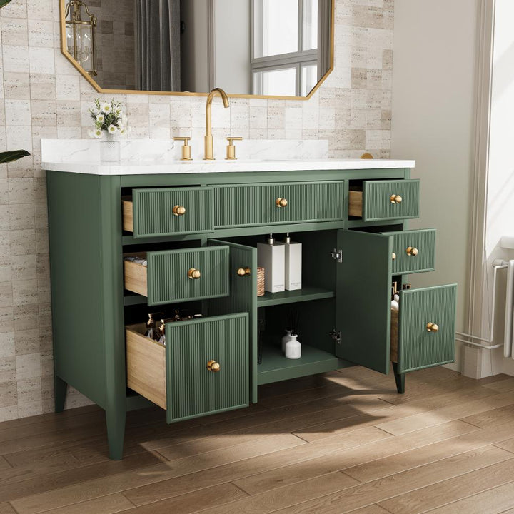 An Aveline 48 Inch Freestanding Bathroom Vanity With Top in green features gold handles and faucet, multiple open drawers and cabinets displaying toiletries and decor, sitting on a wood floor against a tiled wall beneath a crisp white countertop.