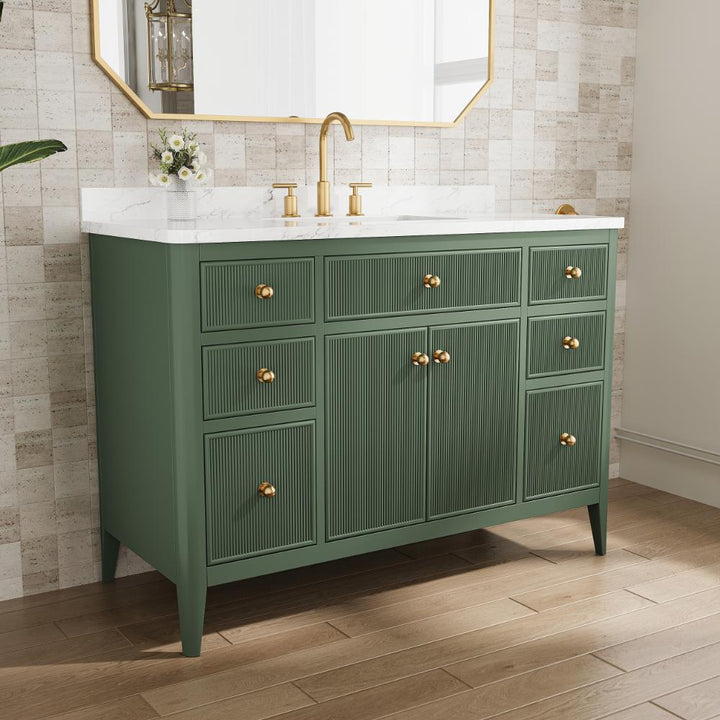 The Aveline 48 Inch Freestanding Bathroom Vanity With Top showcases a green finish, gold hardware, white marble countertop, gold faucet, and floral vase. Six drawers and two cabinets are set against a tiled wall below a large mirror.