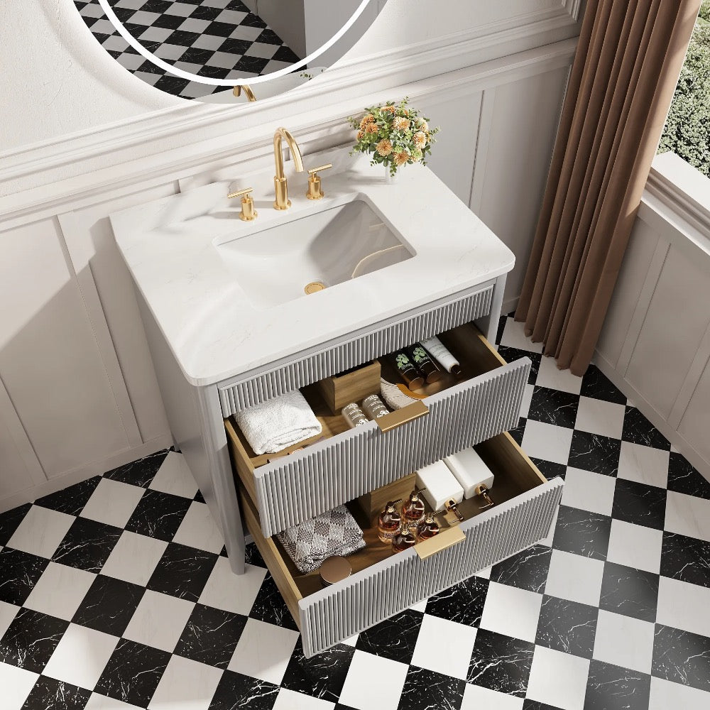 The Aveline 36 Inch Freestanding Bathroom Vanity With Top features a white countertop, gold faucet, under-mount sink, two open drawers for towels and toiletries, and is paired with a round mirror and black-and-white checkered floor.