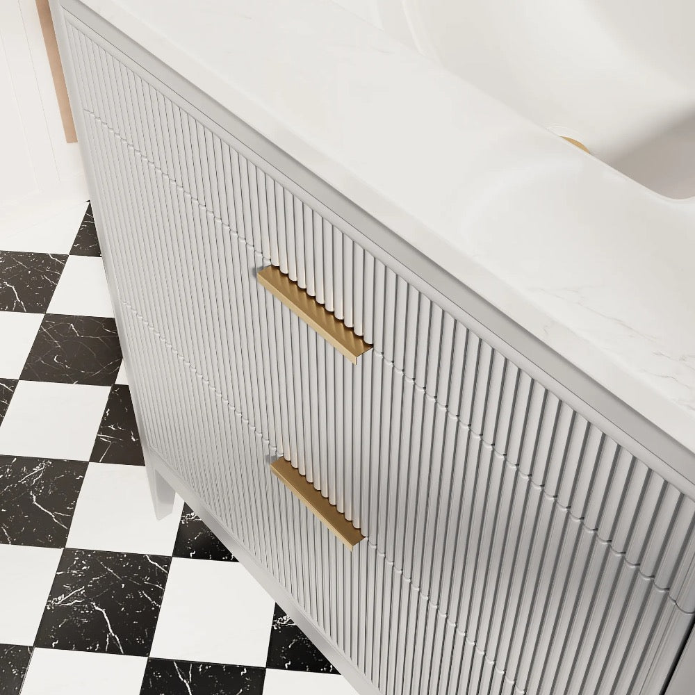 The Aveline 36 Inch Freestanding Bathroom Vanity With Top features vertical ridges, gold handles, and a white marble countertop, and is shown on a striking black and white checkered tile floor.
