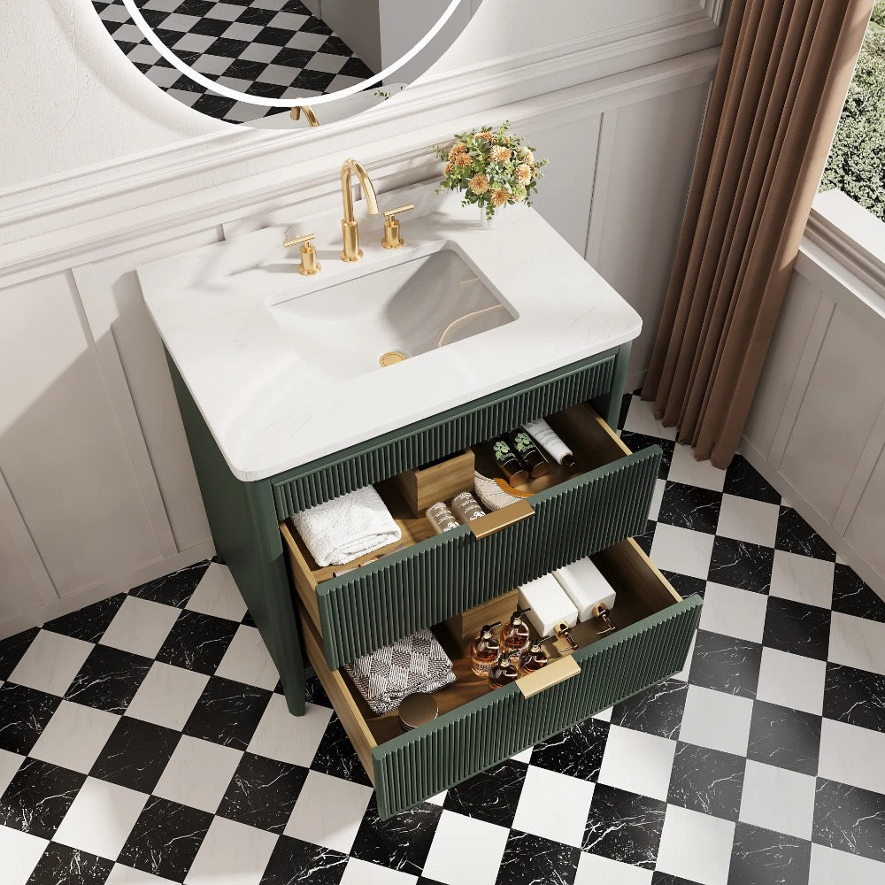 The Aveline 36 Inch Freestanding Bathroom Vanity With Top features a white sink, gold faucet, and three open drawers for storage. Set on a checkered floor, it includes a round mirror and a vase of flowers for added elegance.