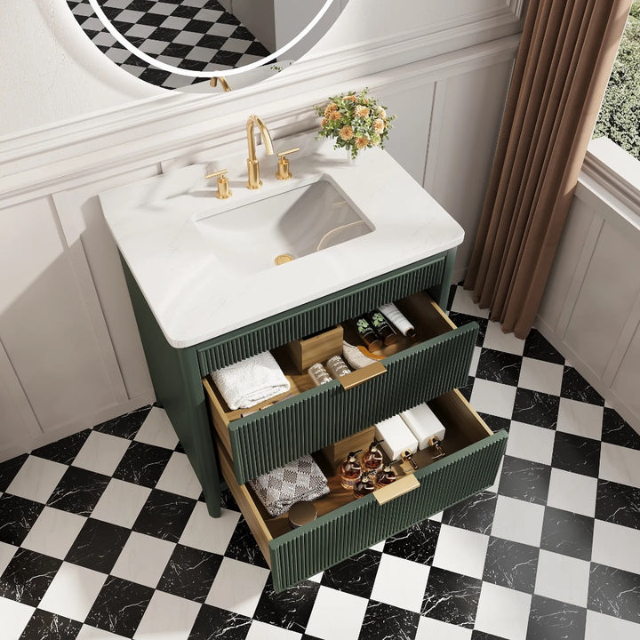 The Aveline 36 Inch Freestanding Bathroom Vanity With Top features a white sink, gold faucet, and three open drawers for storage. Set on a checkered floor, it includes a round mirror and a vase of flowers for added elegance.