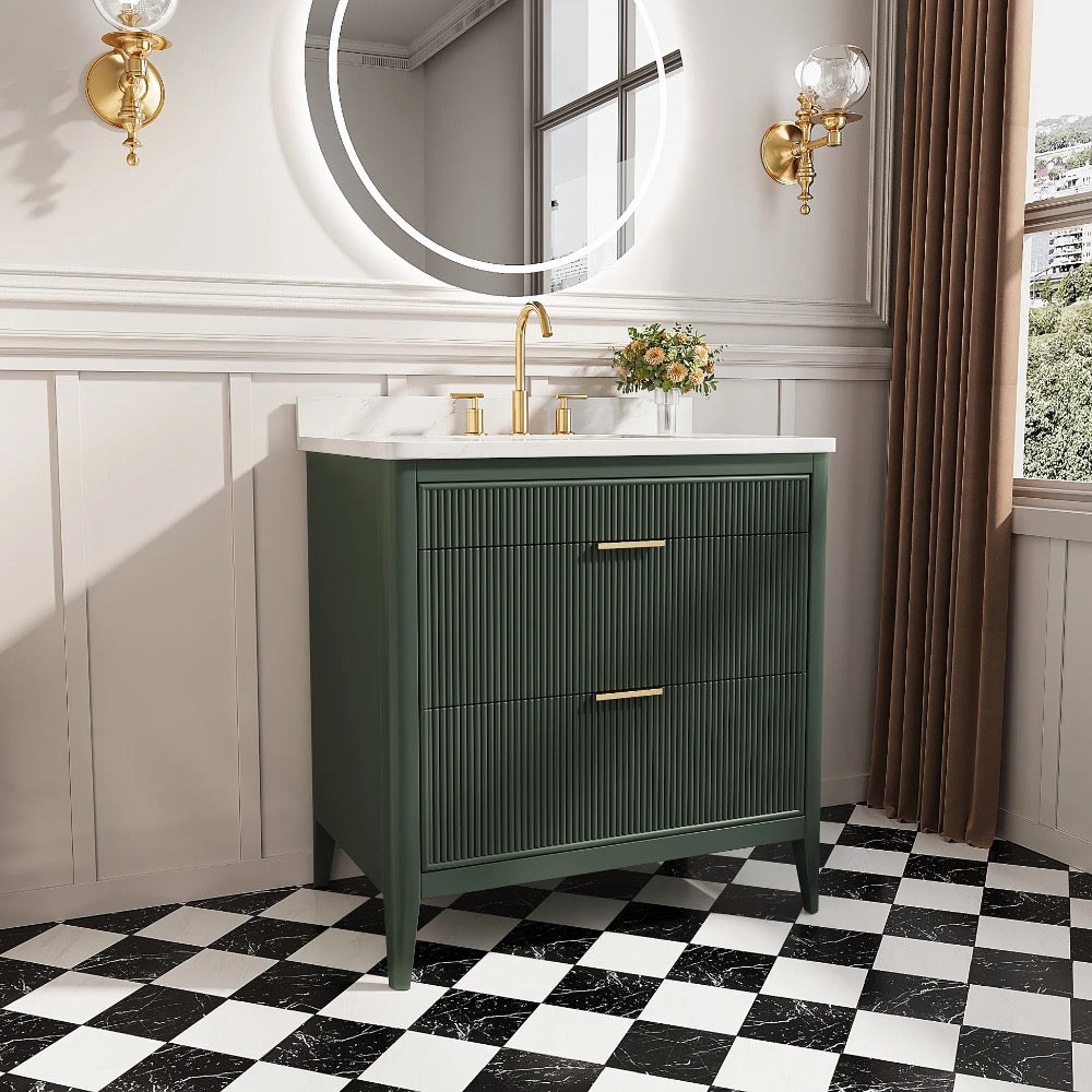 The Aveline 36 Inch Freestanding Bathroom Vanity With Top features a green finish, gold fixtures, and a white countertop, paired with white paneled walls, a round mirror, gold sconces, potted flowers, and checkered floor tiles for modern style.