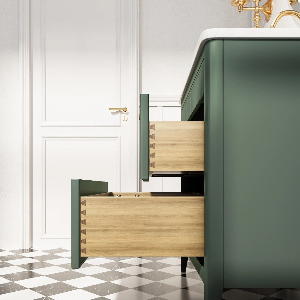 An Aveline 36 Inch Freestanding Bathroom Vanity with Top in green stands on a black and white checkered floor, its two open wooden drawers beside a white door with a gold handle. A white countertop and brass faucet are partially visible above.