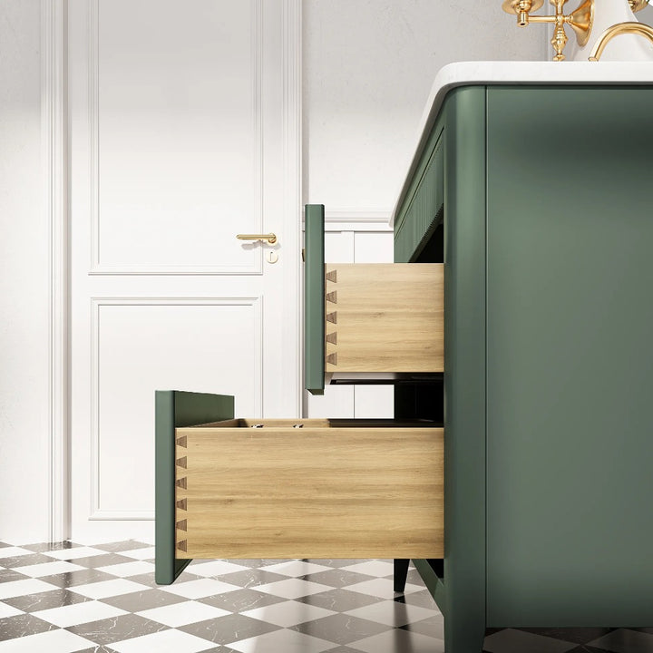 An Aveline 36 Inch Freestanding Bathroom Vanity with Top in green stands on a black and white checkered floor, its two open wooden drawers beside a white door with a gold handle. A white countertop and brass faucet are partially visible above.