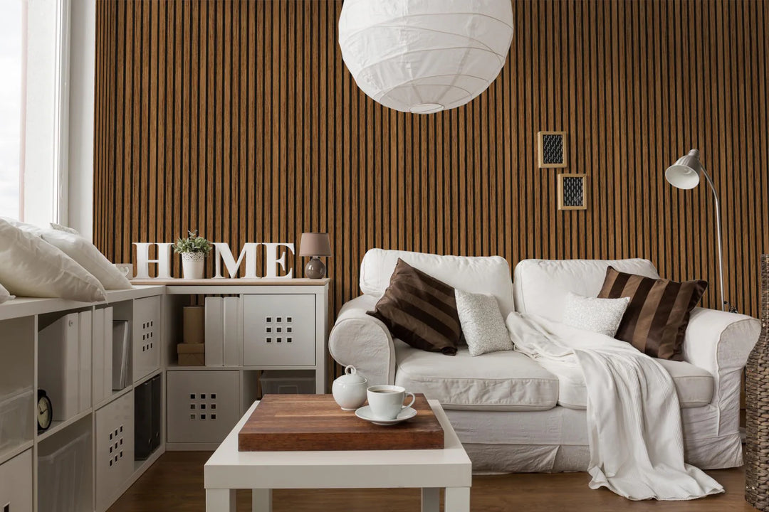 A cozy living room with a white sofa, brown and white cushions, a blanket, a small coffee table with tea set, “HOME” letters, modern shelving, and the Acoustic Interior Wall Panel as an elegant accent.