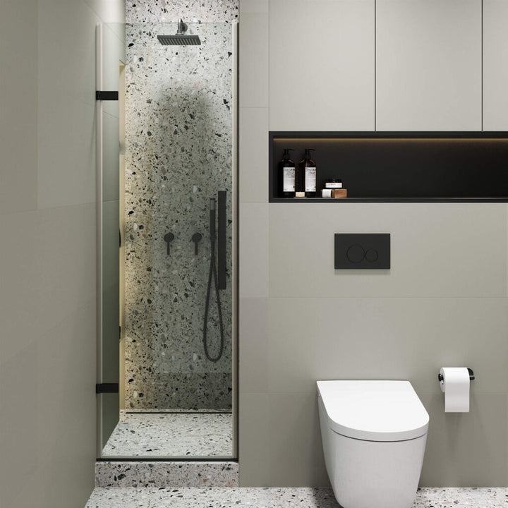 A modern bathroom featuring the Nova Hinged Frameless Shower Door, terrazzo walls and floor, a wall-mounted white toilet, toilet paper holder, black flush plate, and a shelf with bottles and decor.