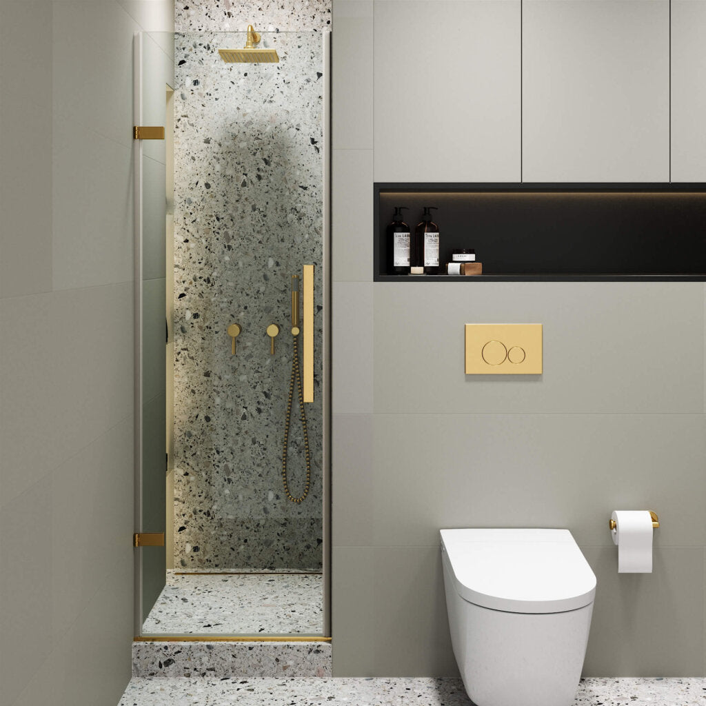 Modern bathroom with a Nova Hinged Frameless Shower Door, terrazzo wall shower and gold fixtures, wall-mounted toilet with gold flush plate, and shelves with toiletries above the toilet.