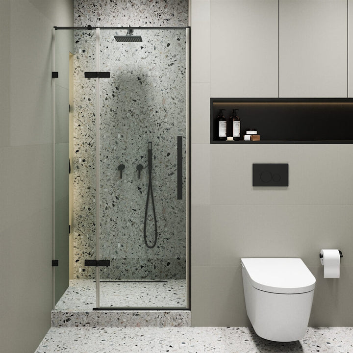 Modern bathroom with a Nova Hinged Frameless Shower Door, terrazzo walls and floor, wall-mounted showerhead, black fixtures, a wall-mounted toilet to the right, toilet paper holder, and shelf with toiletries.