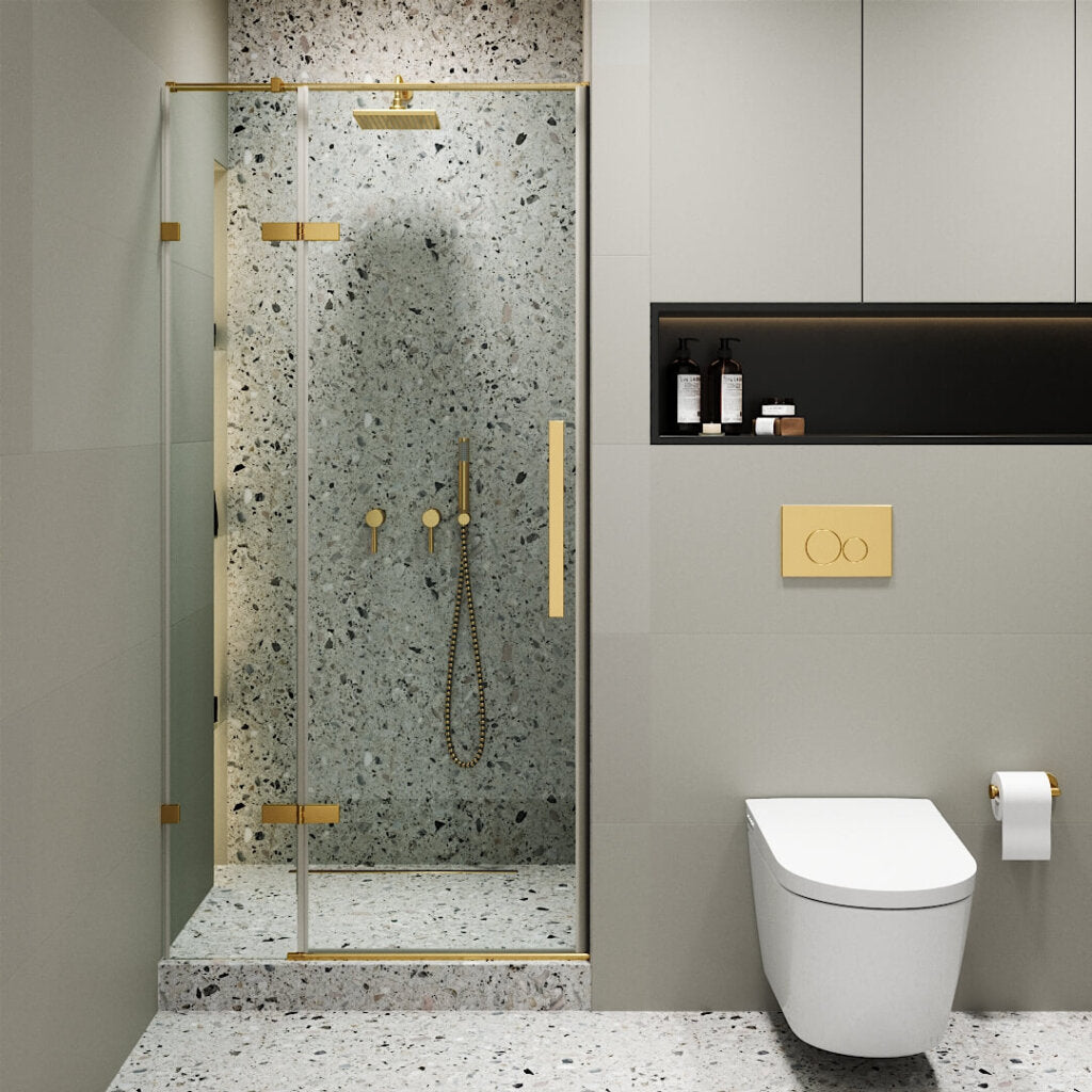 Modern bathroom with the Nova Hinged Frameless Shower Door and gold fixtures, terrazzo walls and floor, a wall-mounted toilet with a gold flush button, plus storage shelves for toiletries.