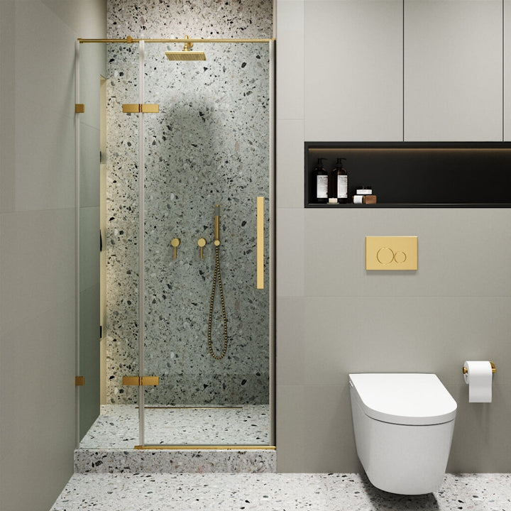Modern bathroom with the Nova Hinged Frameless Shower Door and gold fixtures, terrazzo walls and floor, a wall-mounted toilet with a gold flush button, plus storage shelves for toiletries.
