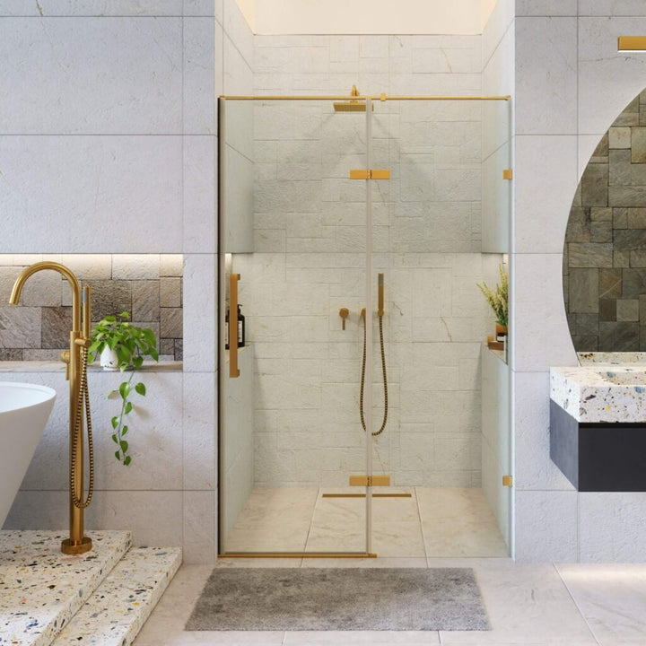 A modern bathroom featuring the Nova Hinged Frameless Shower Door, gold fixtures, a freestanding bathtub, a terrazzo sink, a round mirror, green plants, and light-colored tiles.