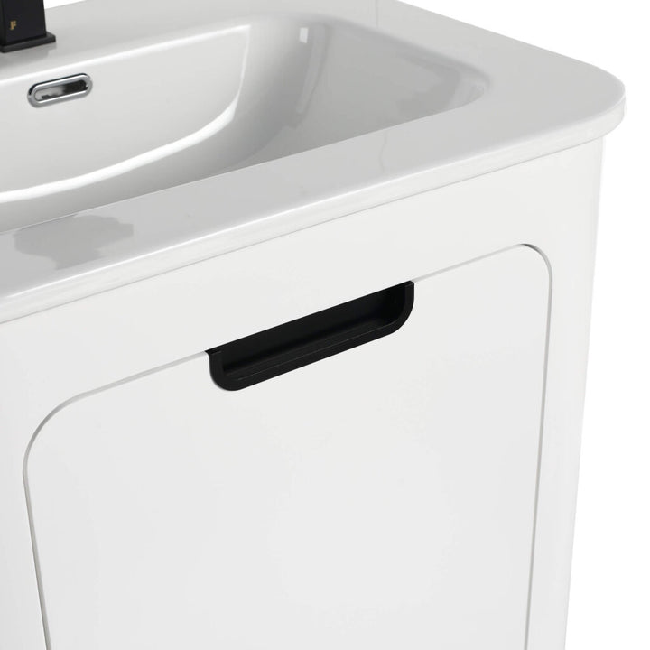 Close-up of the Shireplace 24 Inch Bathroom Vanity, highlighting its white minimalist design. It includes a black cabinet door handle under the integrated sink and a sleek faucet in the background.