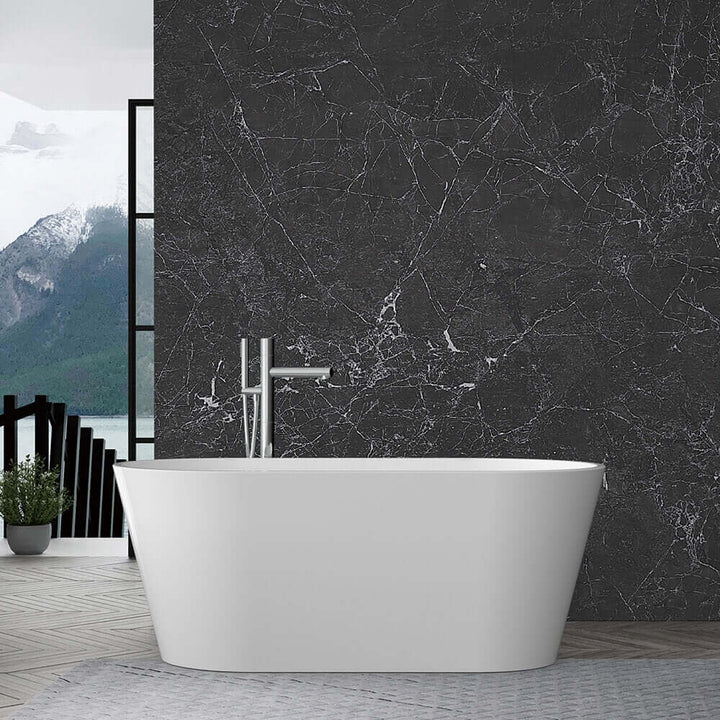 A modern white freestanding bathtub sits in front of a dark marble wall, with a floor-mounted faucet and a mountain view visible through large windows in the background.