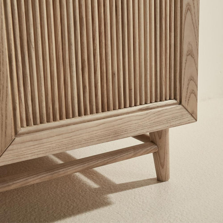 Close-up of the bottom corner of the Liora 30 Inch Bathroom Vanity, featuring vertical wooden slats and natural wood grain, standing on a light-toned textured floor.