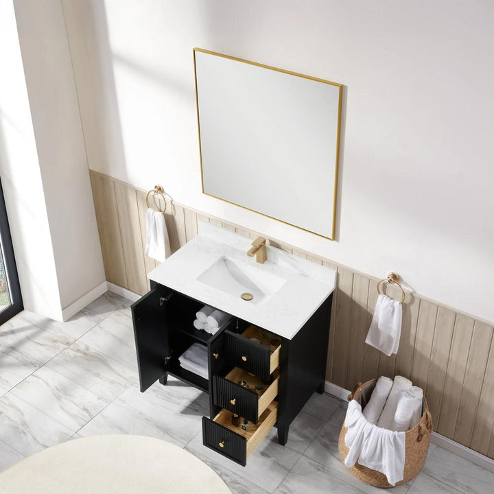 A modern bathroom features the Torino 36 Inch Bathroom Vanity Cabinet with drawers, a white countertop, black finish, and gold faucet. The open cabinet displays towels and toiletries. Nearby are a large mirror, towel rings, and a basket with rolled towels.