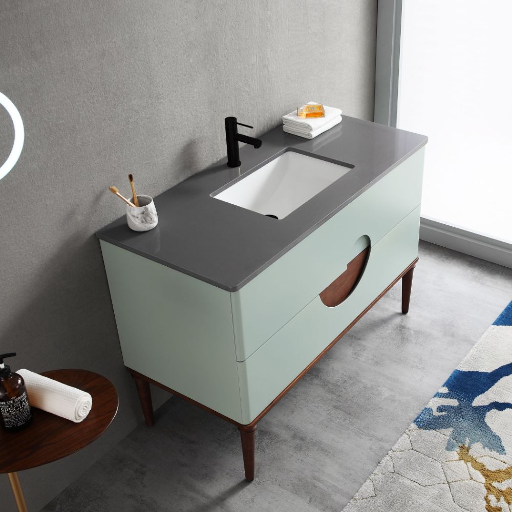 The Burano 48 inch Aloe Green Freestanding Bathroom Vanity features a dark gray countertop, black faucet, built-in sink, and two-tone cabinet. On the counter: a marble cup with toothbrushes, soap dish with soap, and neatly folded towels.