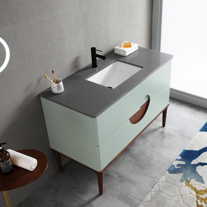 The Burano 48 inch Aloe Green Freestanding Bathroom Vanity features a dark gray countertop, black faucet, built-in sink, and two-tone cabinet. On the counter: a marble cup with toothbrushes, soap dish with soap, and neatly folded towels.