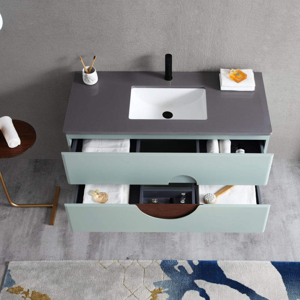 The Burano 48 inch Aloe Green Freestanding Bathroom Vanity features a modern look with an open drawer, gray countertop, white sink, neatly folded towels, and organized soap, toothbrushes, and a decorative tray on the countertop and in the drawers.