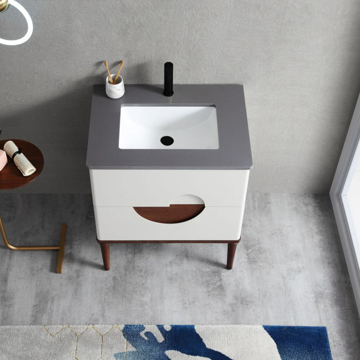 The Burano 30 inch Beige Freestanding Bathroom Vanity features a gray countertop, white rectangular sink, black faucet, and two white drawers on wooden legs. Nearby are a toothbrush holder, towel, and a blue and white rug on the floor.