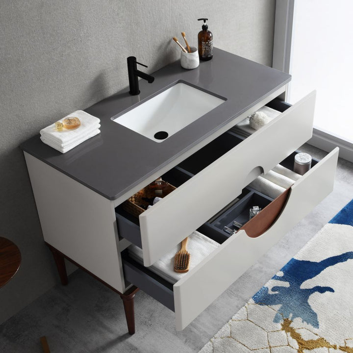 The Burano 48 inch Beige Freestanding Bathroom Vanity features a modern gray countertop, black faucet, white sink, open drawers with towels and toiletries, and a partially visible blue and beige rug.
