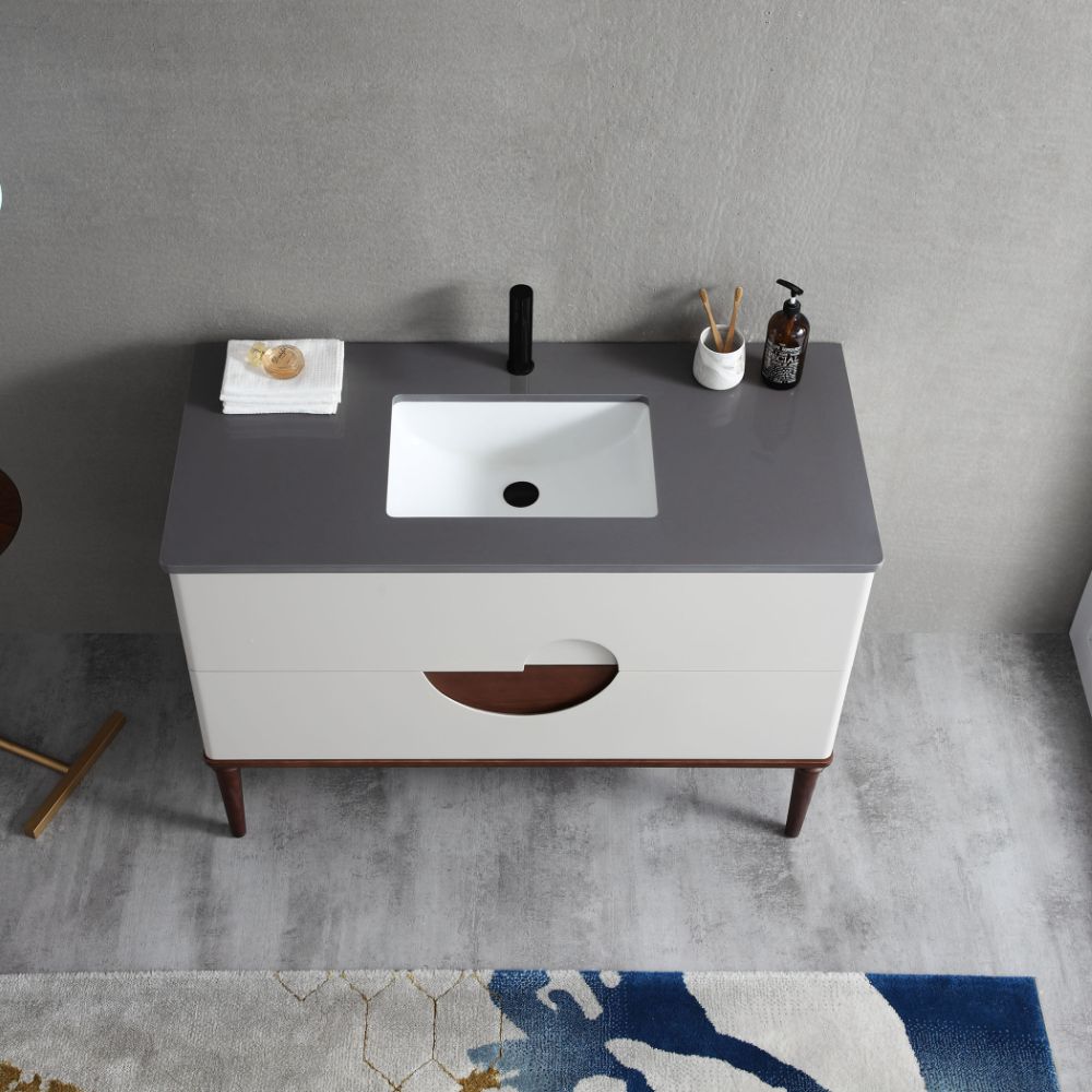 The Burano 48 inch Beige Freestanding Bathroom Vanity has a gray countertop, white rectangular sink, black faucet, soap dispenser, folded towel, and soap. It includes two drawers and wooden legs on a gray floor next to a colorful rug.