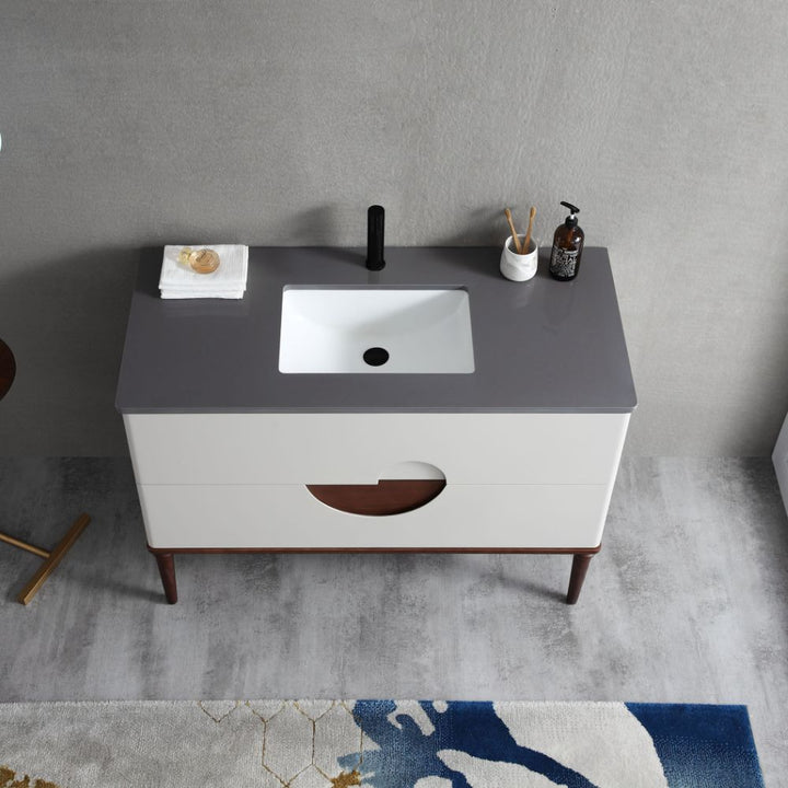 The Burano 48 inch Beige Freestanding Bathroom Vanity has a gray countertop, white rectangular sink, black faucet, soap dispenser, folded towel, and soap. It includes two drawers and wooden legs on a gray floor next to a colorful rug.