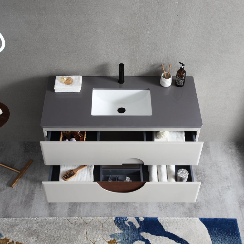 The Burano 48 inch Beige Freestanding Bathroom Vanity features a gray countertop, white sink, black faucet, soap dispenser, toothbrush holder, plus two drawers for towels and toiletries. A rug and stool are partially visible below.