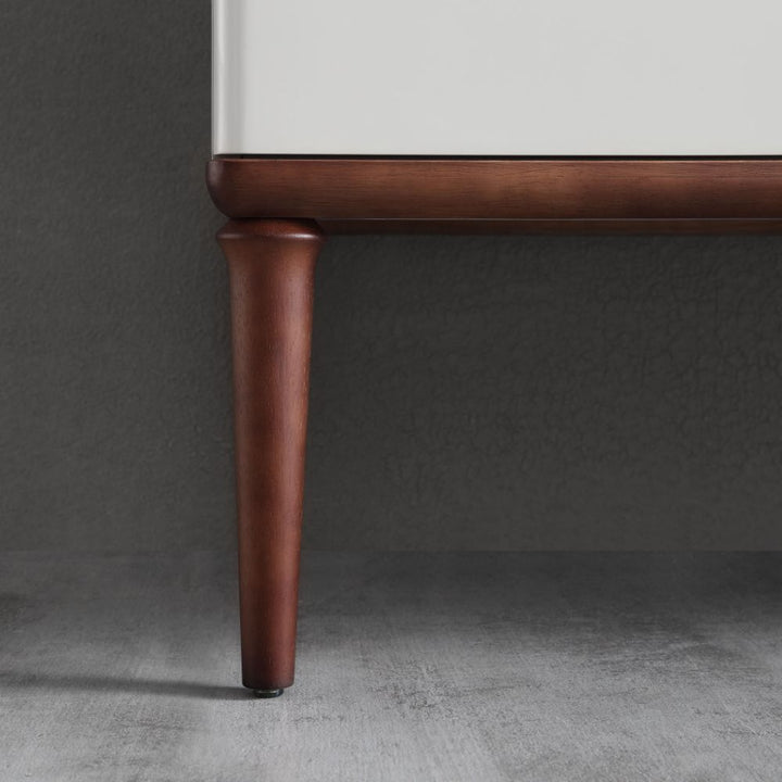 Close-up of an Burano 48 inch Beige Freestanding Bathroom Vanity leg, crafted from dark wood and attached to a white side panel, shown on a gray textured floor against a gray wall.