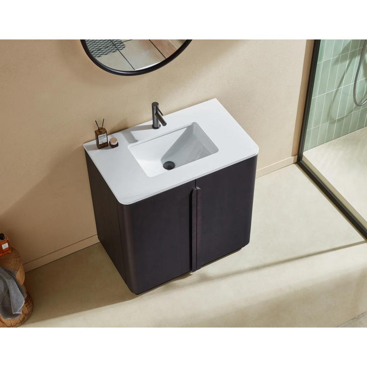 The Parma 36 Inch Bathroom Vanity With Top includes a white rectangular sink, black faucet, and dark cabinet, positioned beneath a round mirror on a beige wall. Toiletries are neatly arranged on the vanity surface.