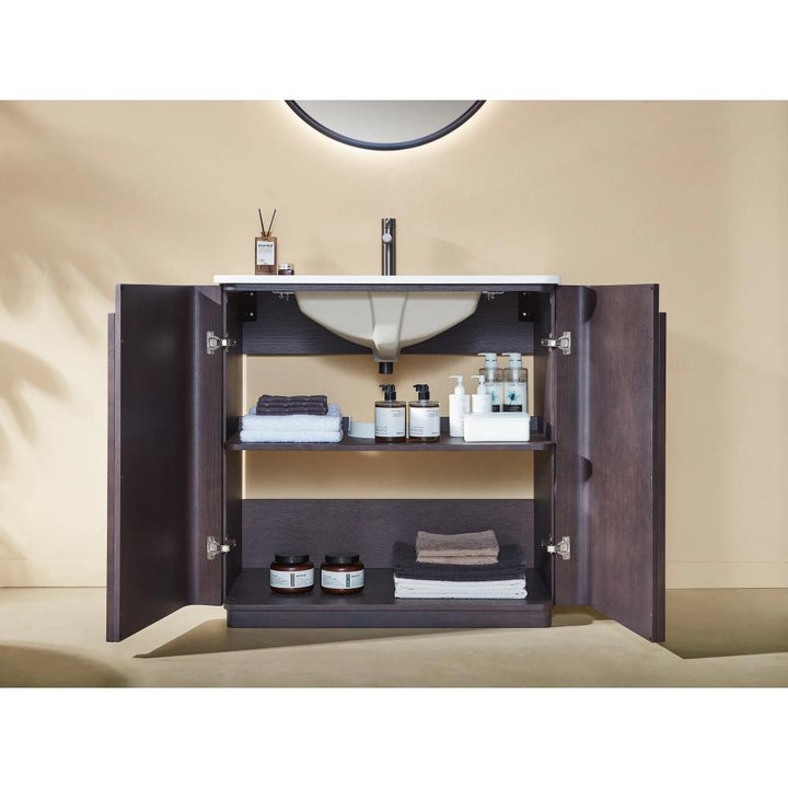 The Parma 36 Inch Bathroom Vanity With Top is shown with both doors open, neatly displaying towels, bottles, jars, and toiletries on its shelves beneath a white sink and a round mirror.
