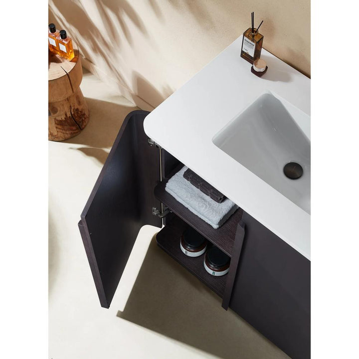 The Parma 36 Inch Bathroom Vanity With Top showcases an open dark wood cabinet with folded towels and storage jars below a white sink, while soap, a dispenser, and a reed diffuser sit on the countertop.