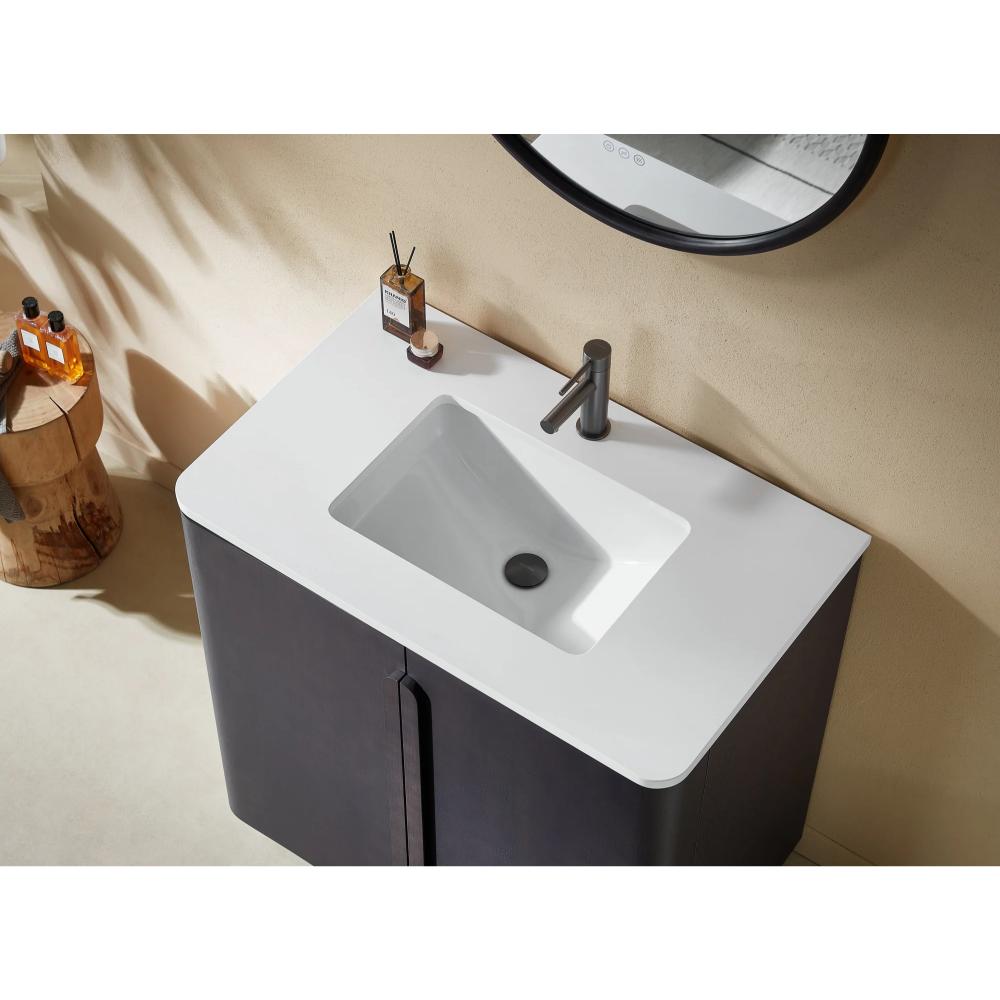 The Parma 36 Inch Bathroom Vanity With Top includes a white rectangular sink, black faucet, and dark cabinet, with a soap dispenser and reed diffuser on the counter. A round mirror and wooden side table with bottles are nearby.