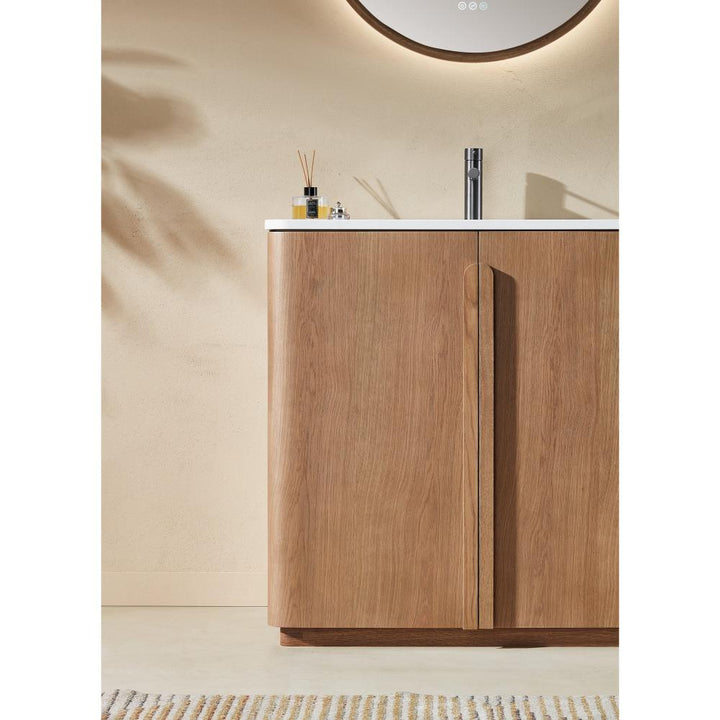 The Parma 36 Inch Bathroom Vanity With Top boasts light wood cabinet doors, a white countertop, a silver faucet, and minimal accessories, with soft lighting and a round mirror above.
