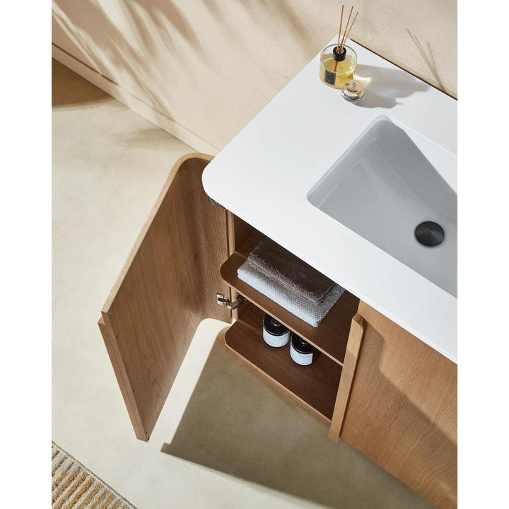 The Parma 36 Inch Bathroom Vanity With Top has a white sink and an open wooden cabinet with shelves for towels and bottles, accented by a reed diffuser and candle on the counter, all against beige floors and walls.