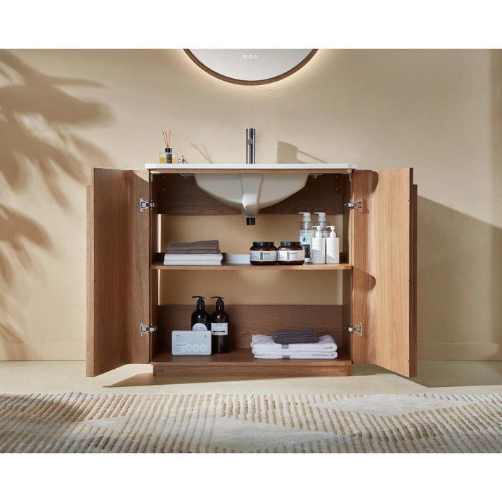 A Parma 36 Inch Bathroom Vanity With Top, set against a beige wall, displays open wooden doors revealing shelves with towels and toiletries under a white sink, complemented by a patterned rug on the floor.