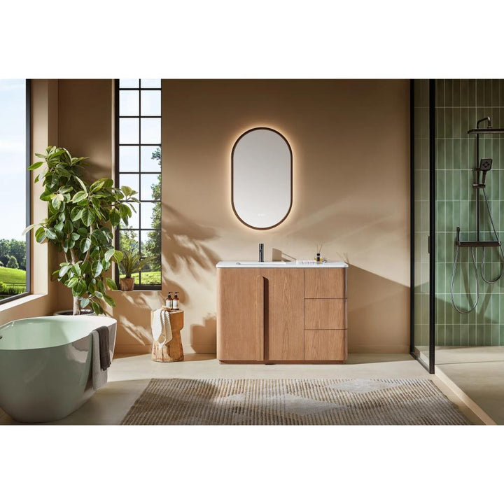 Modern bathroom with a green bathtub, Parma 48 Inch Bathroom Vanity With Top, oval backlit mirror, indoor plant, and glass shower. Large windows bring in natural light, and neutral tones with minimal decor create a serene vibe.