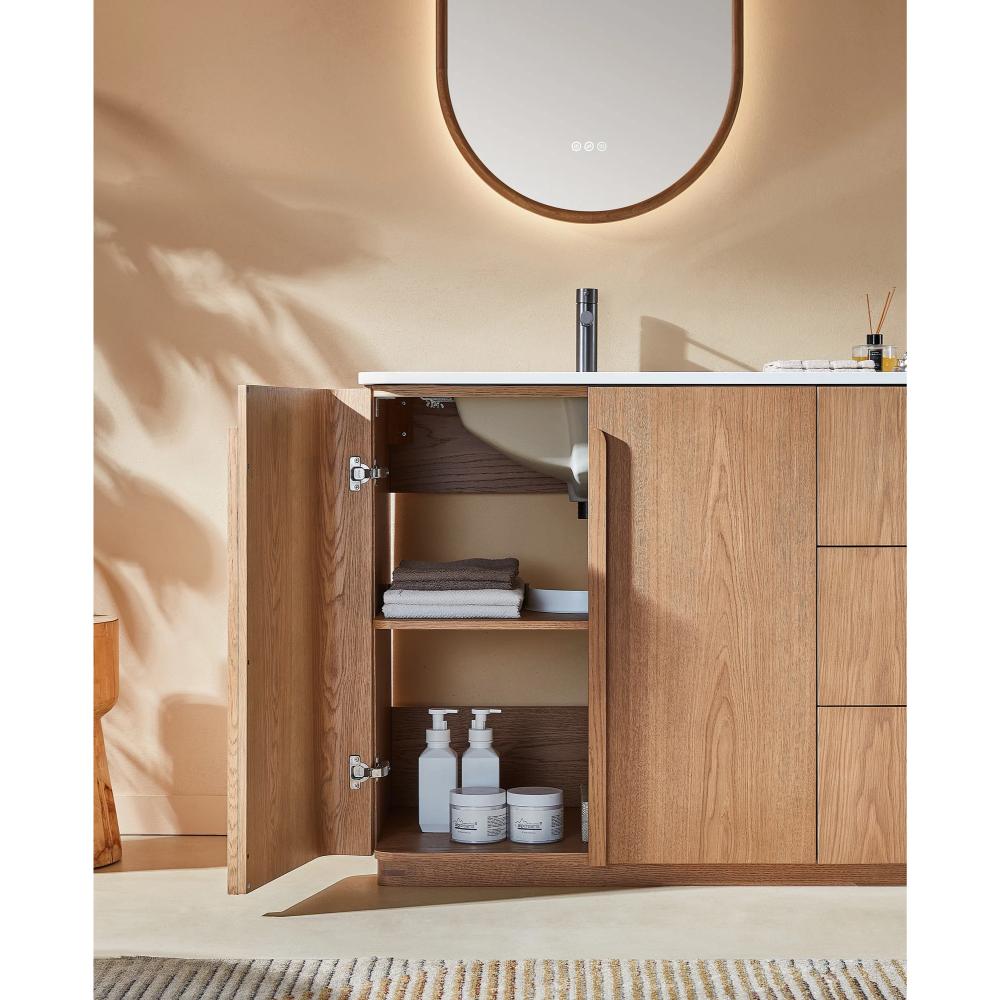 A modern Parma 48 Inch Bathroom Vanity With Top features light wood cabinets. The left door is open, revealing neatly folded towels and bottles inside. Above is a white sink with a black faucet and an oval mirror on the wall.