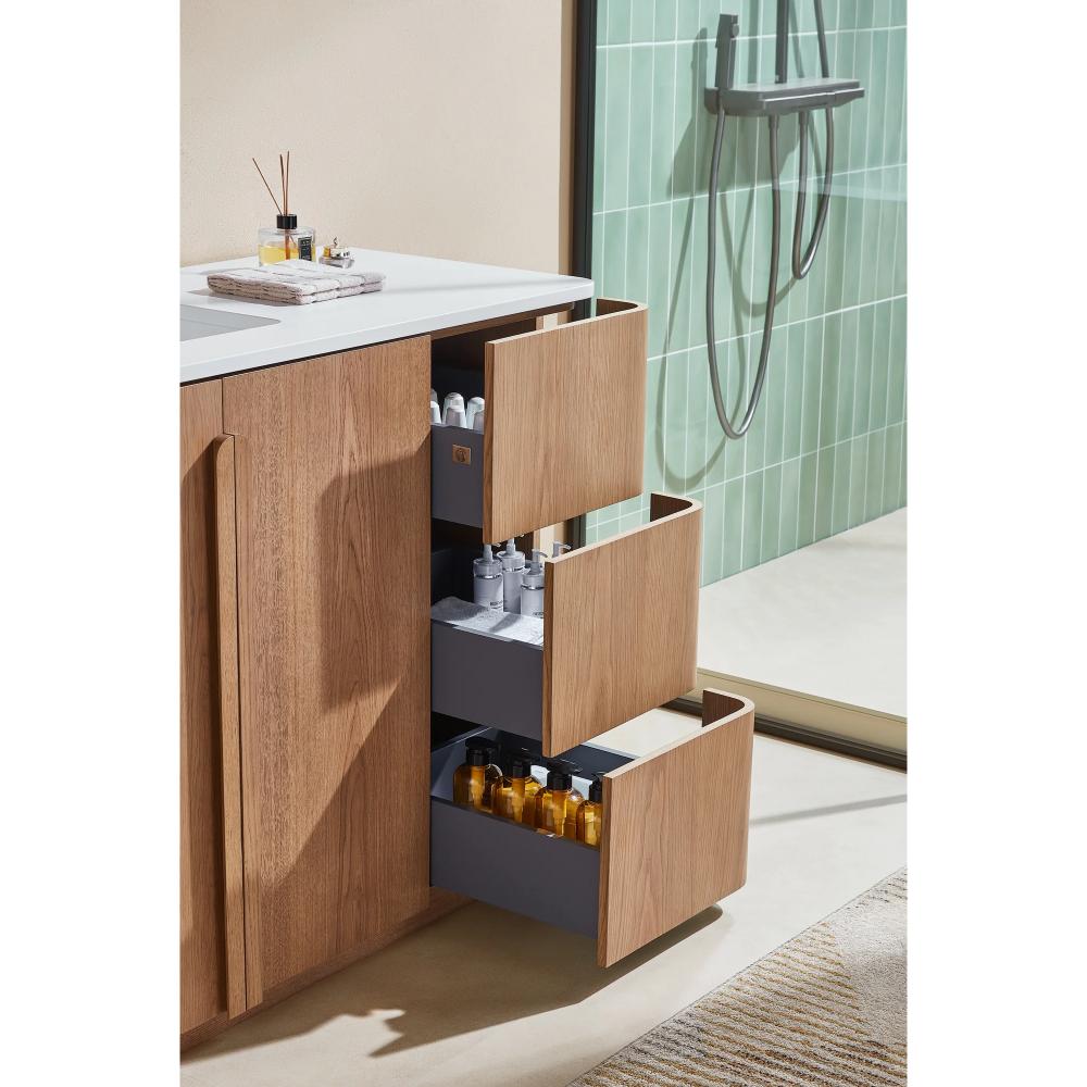 A Parma 48 Inch Bathroom Vanity With Top includes three open gray drawers holding bottles and toiletries. A glass shower with green tile walls is on the right, and a beige rug lies on the floor.