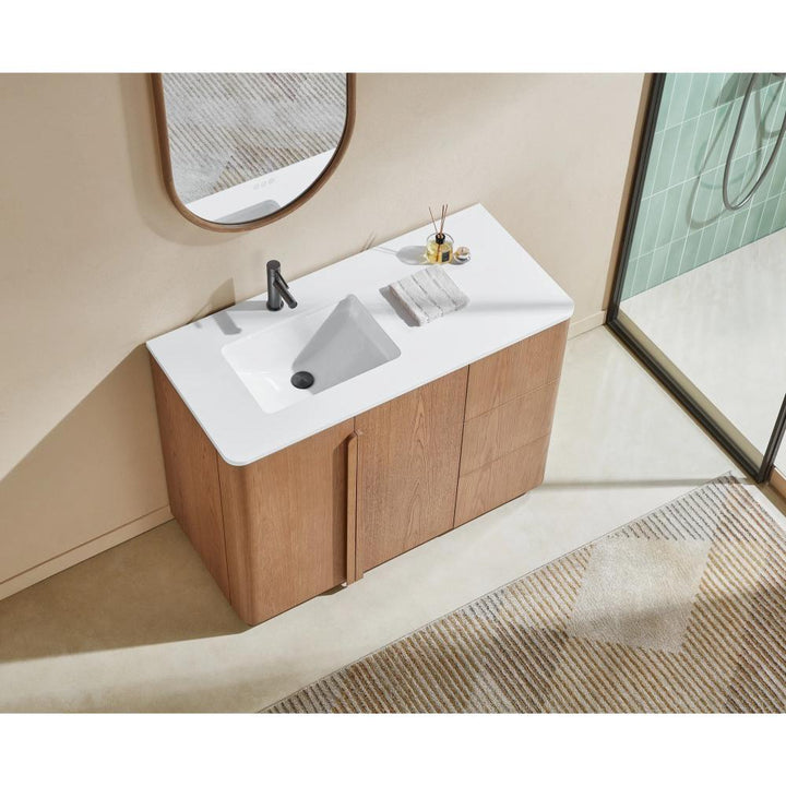 The Parma 48 Inch Bathroom Vanity With Top features a white rectangular sink, light wood cabinet, black faucet, towel, and toiletries. A frameless mirror hangs above, with a glass shower to the right and a patterned rug on the floor.