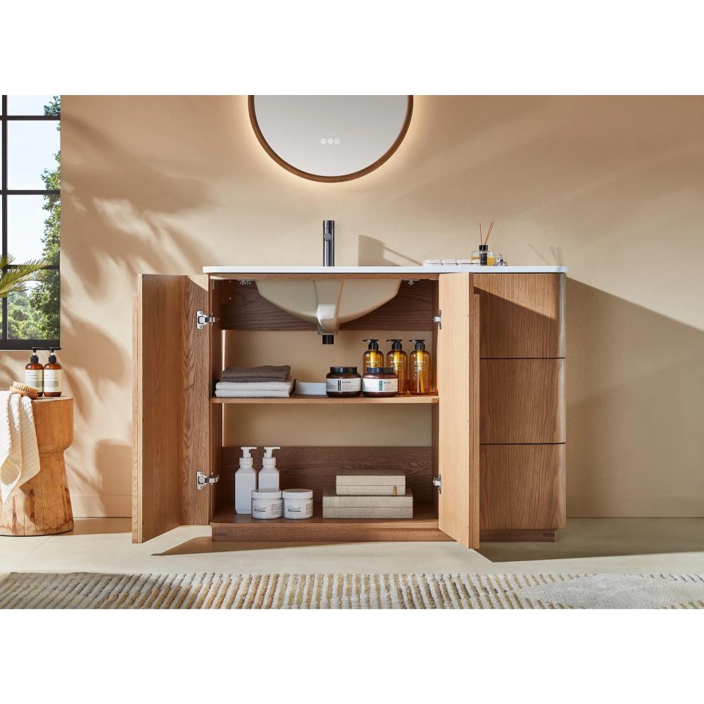 A Parma 48 Inch Bathroom Vanity With Top stands with open cabinet doors, showing neatly organized towels, cleaning products, and toiletries inside. On the white countertop above are a round mirror, soap dispensers, and toothbrush holders.