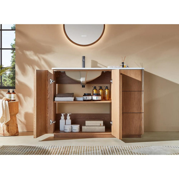A Parma 48 Inch Bathroom Vanity With Top stands with open cabinet doors, showing neatly organized towels, cleaning products, and toiletries inside. On the white countertop above are a round mirror, soap dispensers, and toothbrush holders.