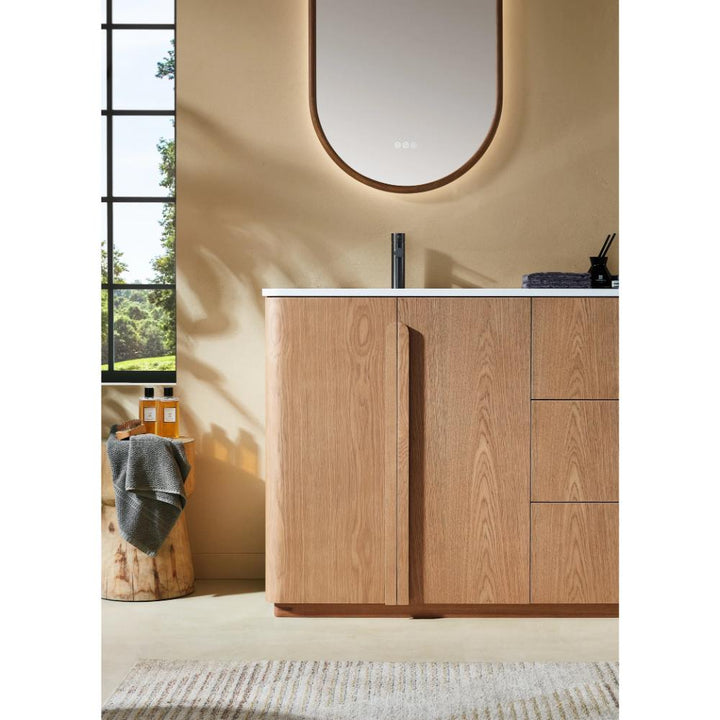 A modern bathroom featuring the Parma 72 Inch Double Bathroom Vanity With Top, black faucet, oval mirror, and a window framing greenery. A gray towel and toiletries rest on a wooden stool beside the vanity.