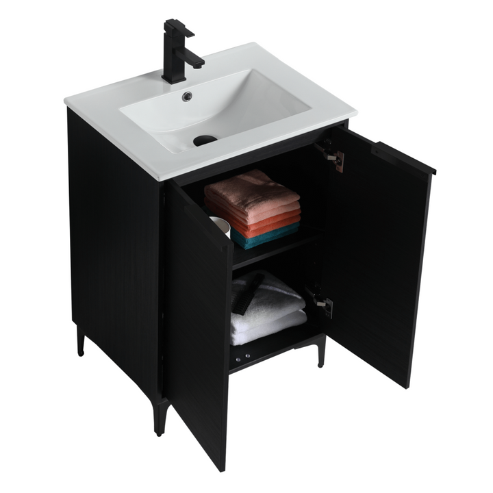 The Wilmington 24 Inch Bathroom Vanity With Sink has an open cabinet showing folded towels in white, pink, and teal. Its black design includes a sleek white sink top and modern black faucet, complementing a crisp white backdrop.